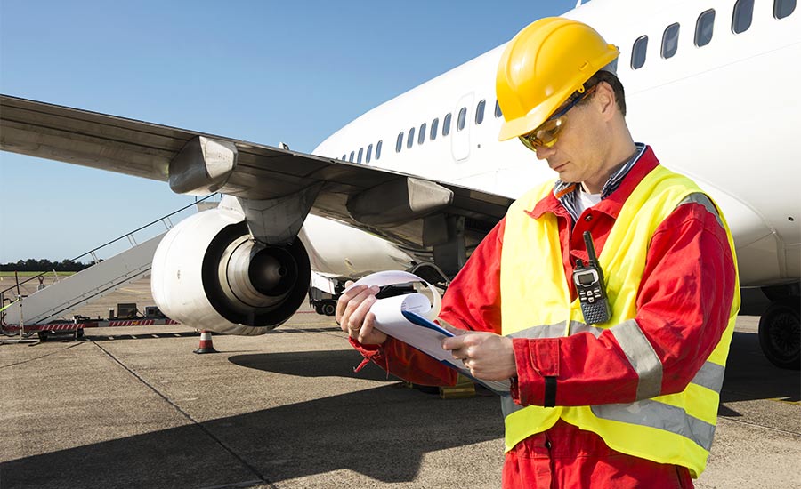 An aircraft engineer with documents in his hands next to an airplane​