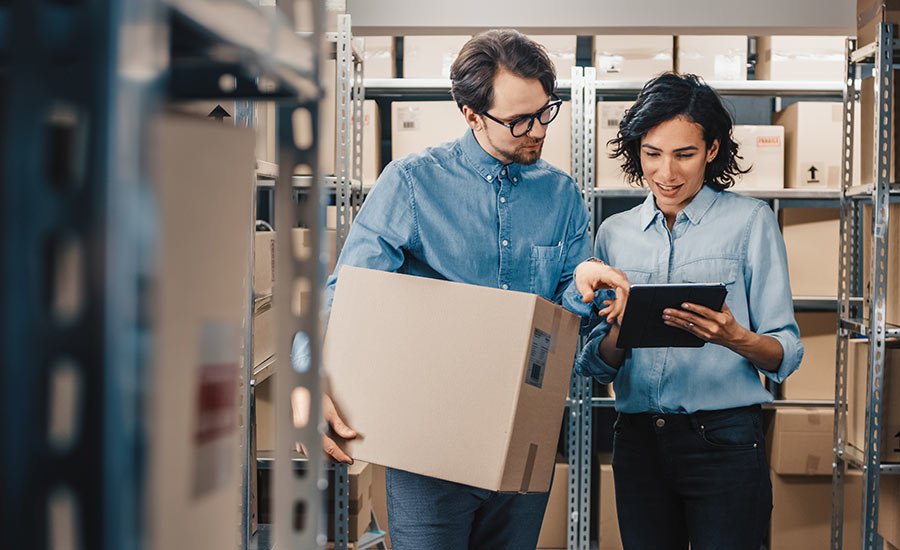 An inventory manager with a tablet next to a worker holding a cardboard box​